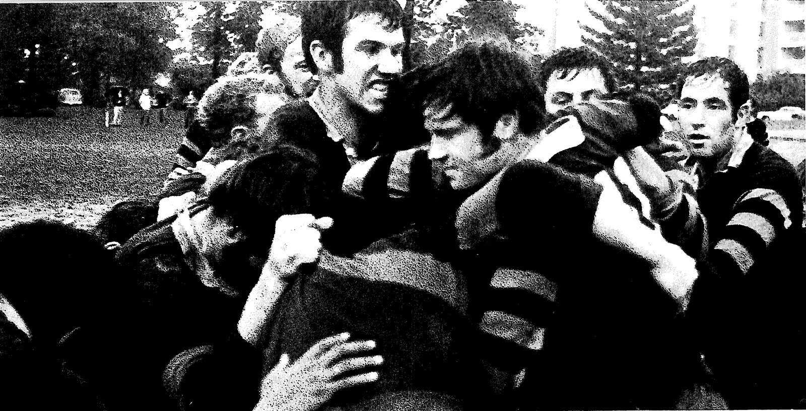 Black and white photograph of Mizzou forwards in hooped jerseys packed together in a ruck, trees and a tall building behind them