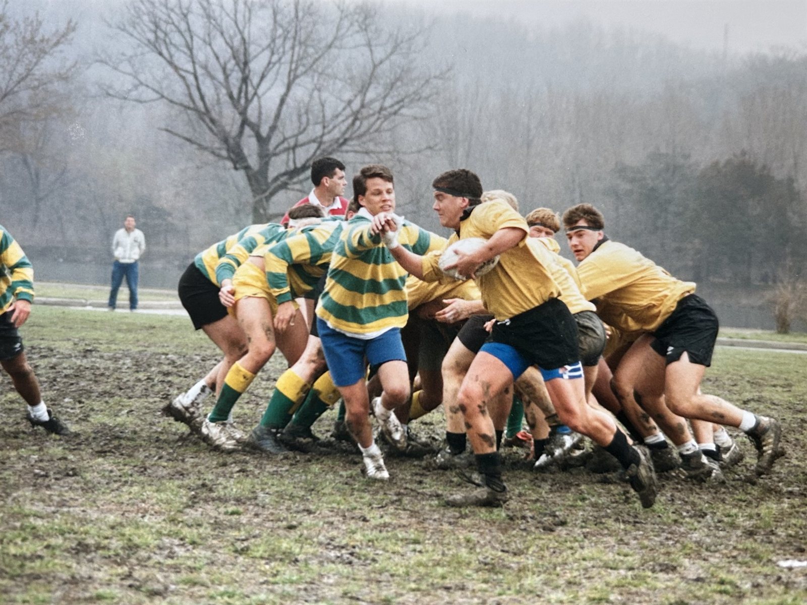 Mizzou forwards in gold jerseys drive a maul forward against a green-and-gold hooped side on a churned-up pitch during the 1990-91 season