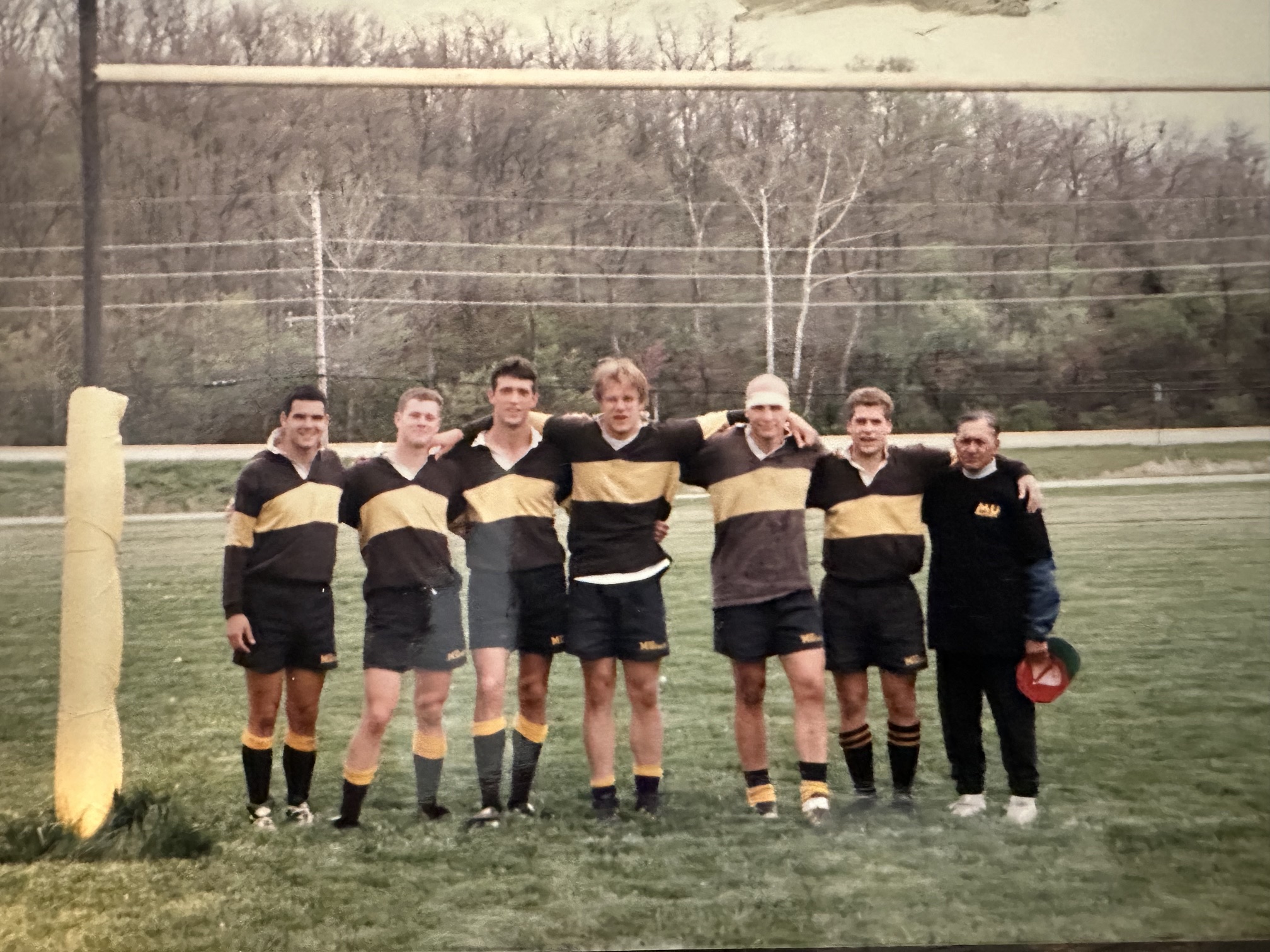 Seven men standing arm in arm in front of the goalposts in Mizzou black and gold hooped jerseys after the final match of the 1996-97 season