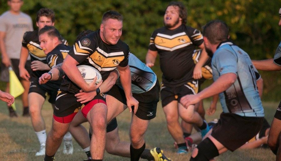 A Mizzou ball carrier in black and gold chevron kit breaks through a tackle against a side in pale blue