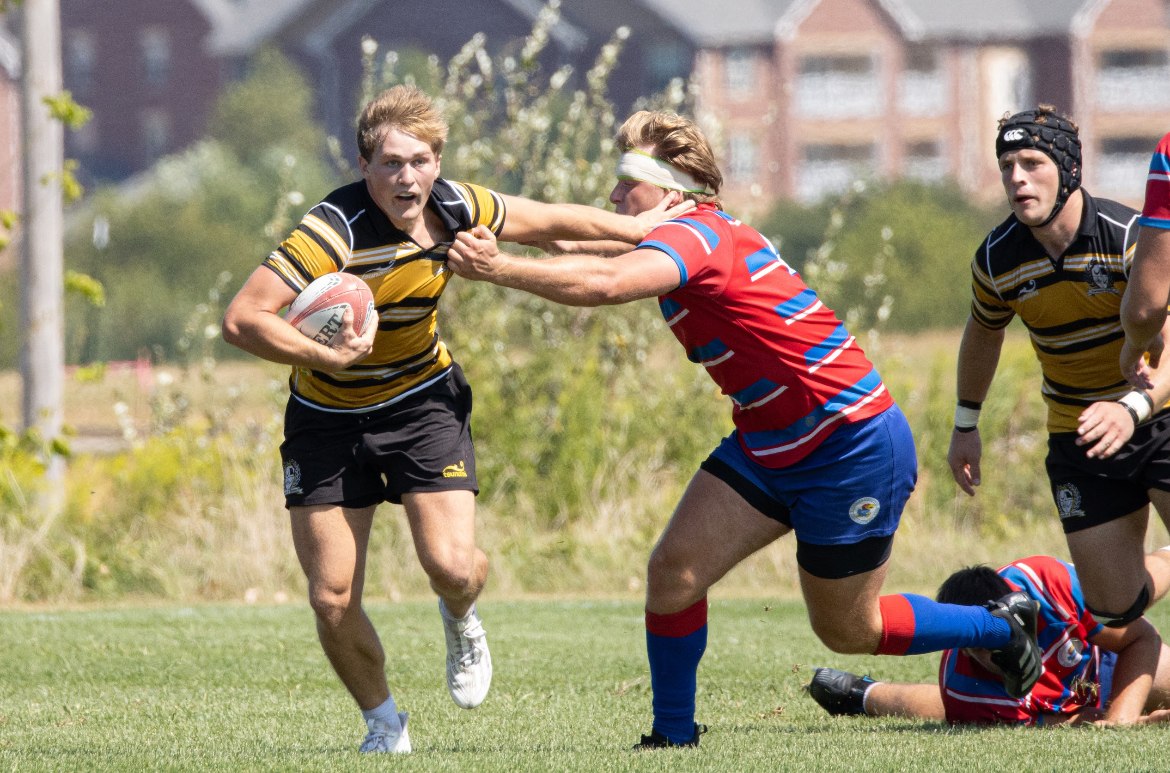 Mizzou inside center Drew Blomquist, in black and gold hoops, hands off a red-and-blue opponent while carrying the ball at Gans Creek Recreation Area