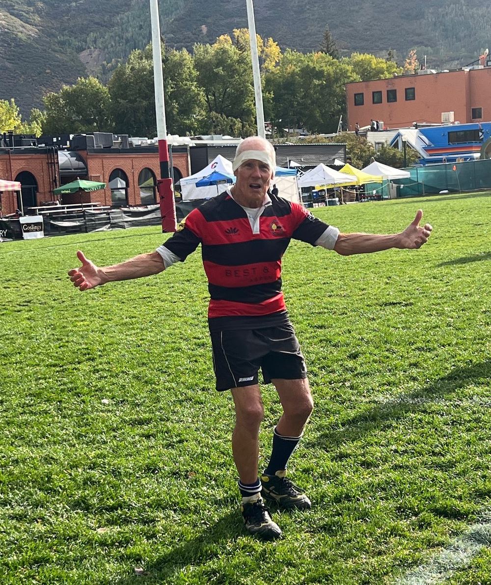 Jim Dierker on the pitch at Aspen in 2025, arms spread wide, wearing a red and black hooped jersey and a bandage around his head