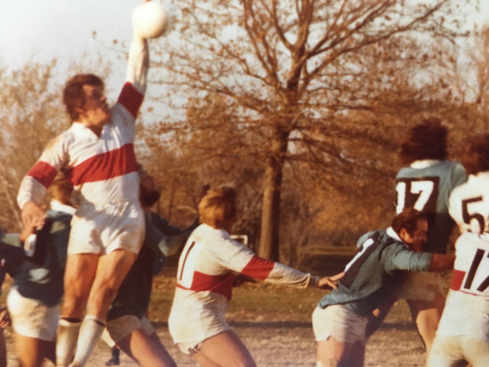 Color photograph of a lineout, a Missouri Rugby Union player in a red-hooped jersey reaching high to take the ball against Colorado