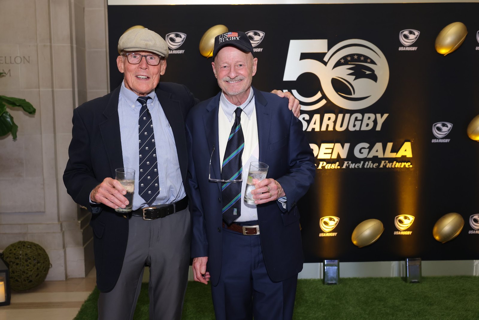 Jim Dierker and Rick Wetzel in suits at the USA Rugby 50th anniversary gala, standing in front of a branded backdrop