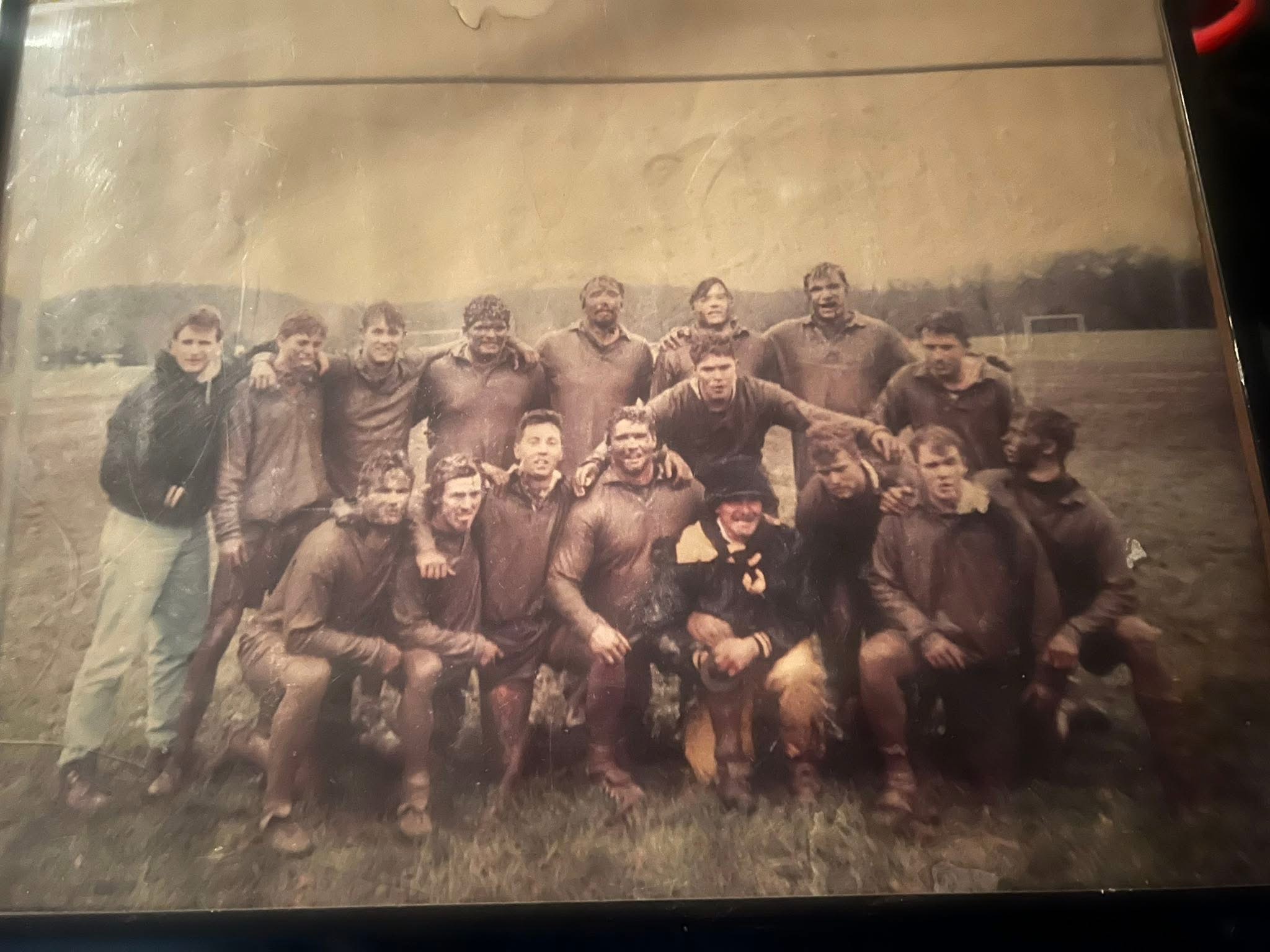 Mud-covered Mizzou rugby squad posing together after a match in the club's early years