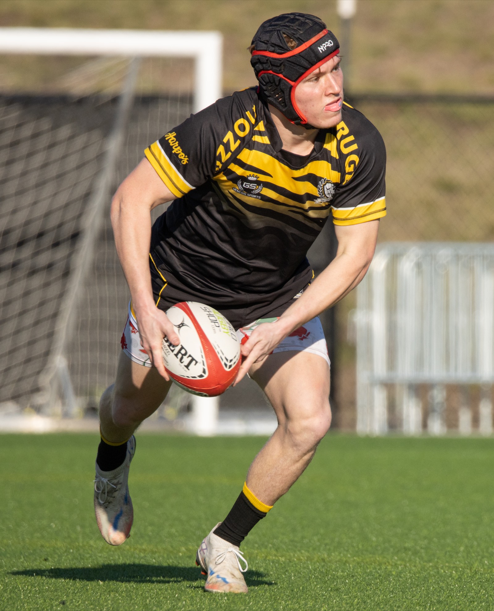 A Mizzou player in a red scrum cap runs with the ball on a turf pitch