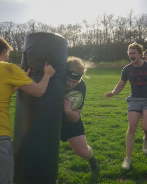 A Mizzou player drives shoulder-first into a tackle bag held by a teammate during spring 2025 training