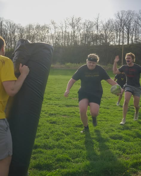 A Mizzou player carrying the ball runs at a tackle bag during a spring 2025 training session while teammates cheer him on