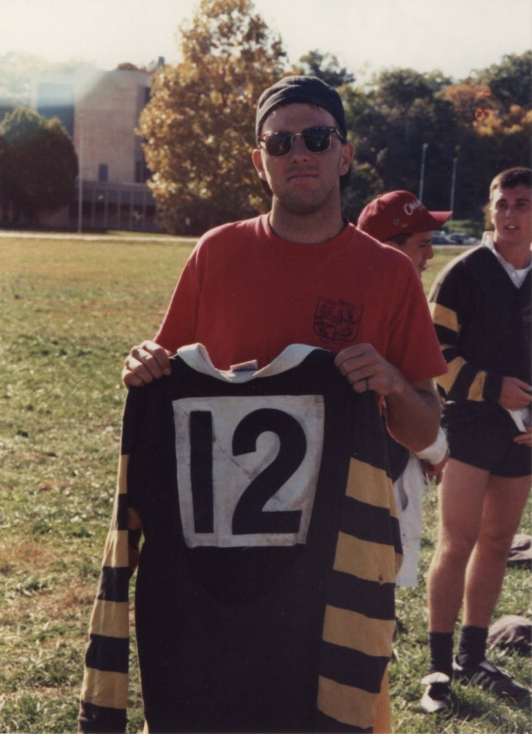 Chris Justice holds up a black and gold hooped jersey numbered 12