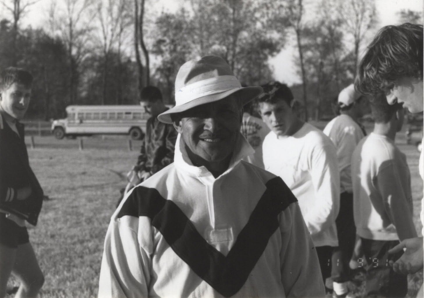 Coach Ian Hermann smiling on the touchline among players, black and white photograph