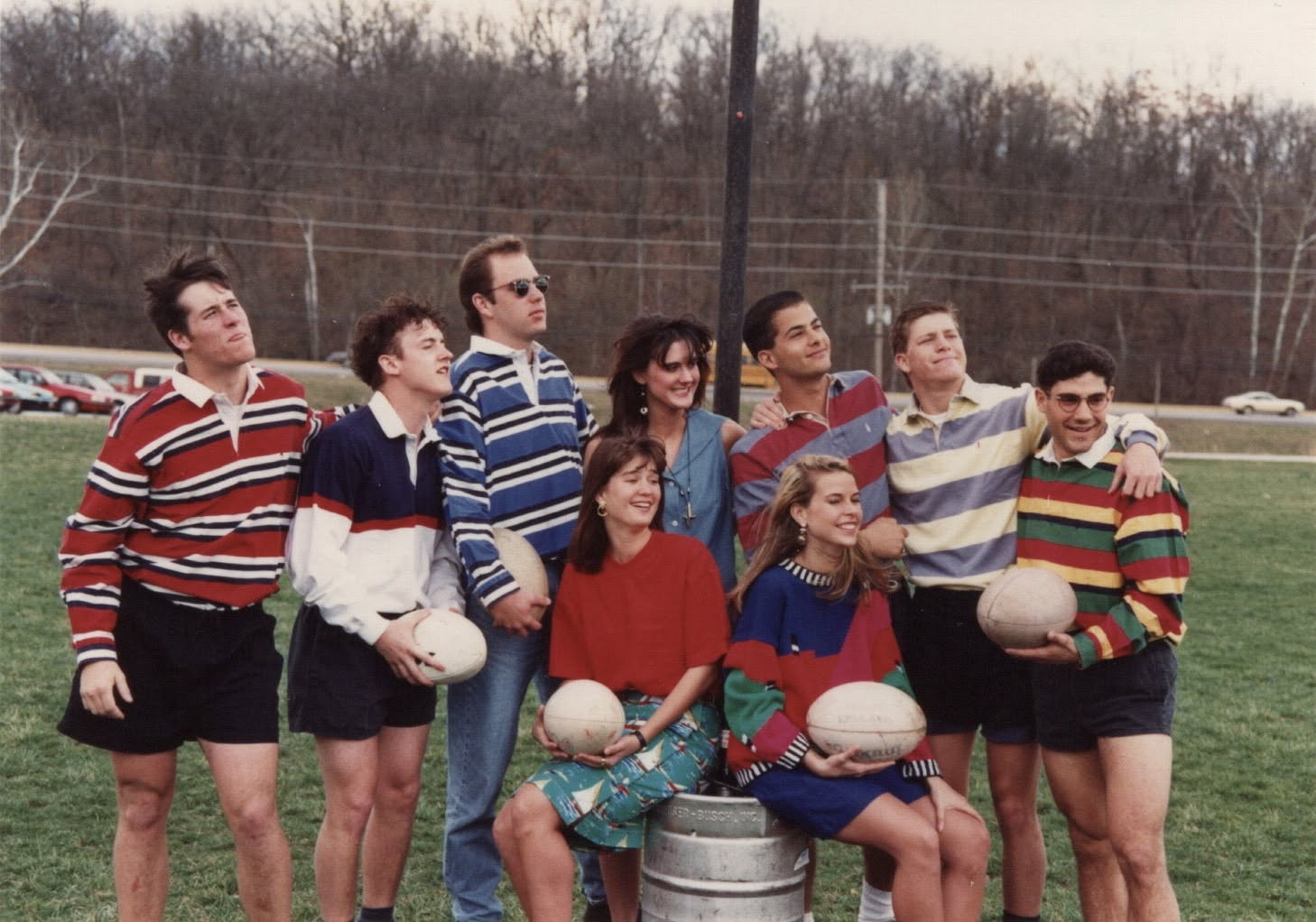 A group in striped rugby shirts posed with match balls and a keg