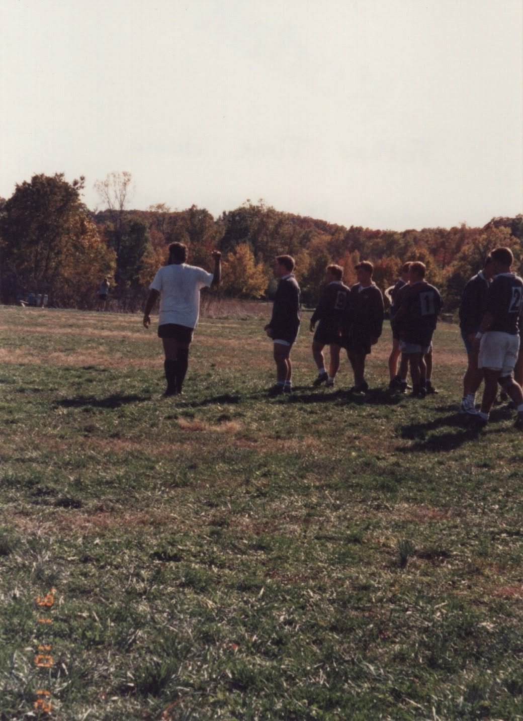 Players walk across a pitch ringed by autumn trees