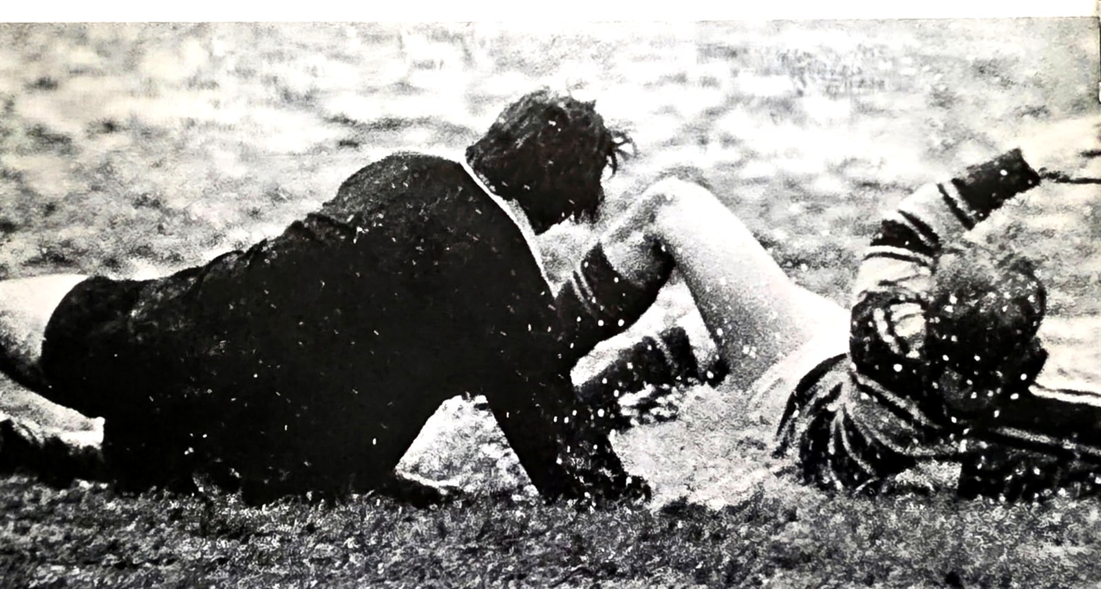 Two rugby players on the ground in deep mud after a tackle, from the Savitar yearbook rugby page