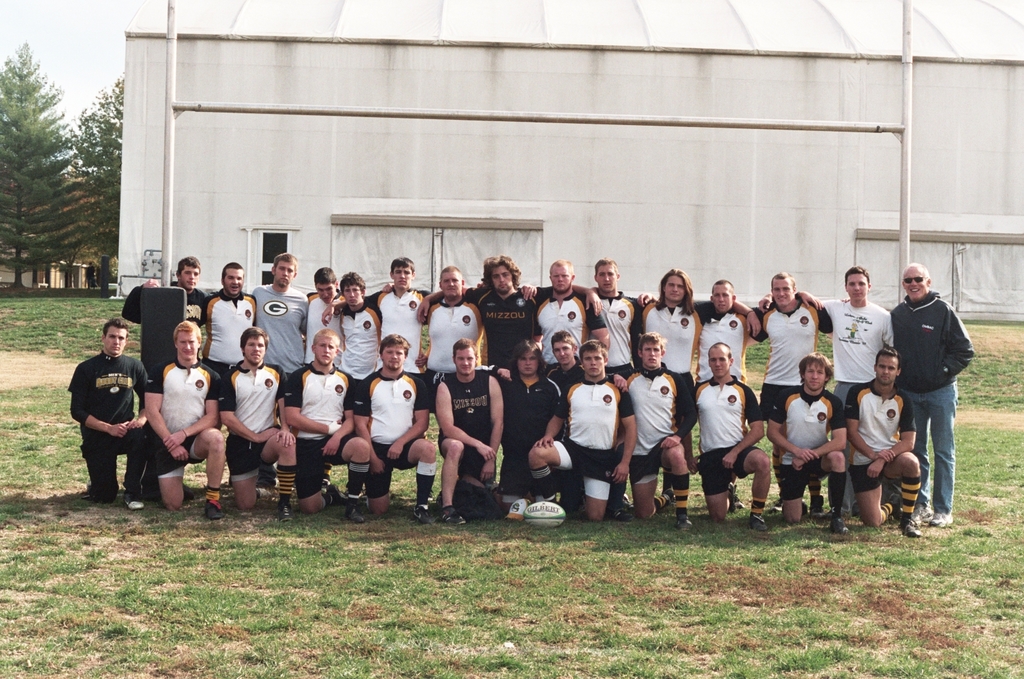 The 2006-07 Mizzou rugby squad posed in two rows on the practice field, in white and black Mizzou jerseys, in front of the domed practice facility